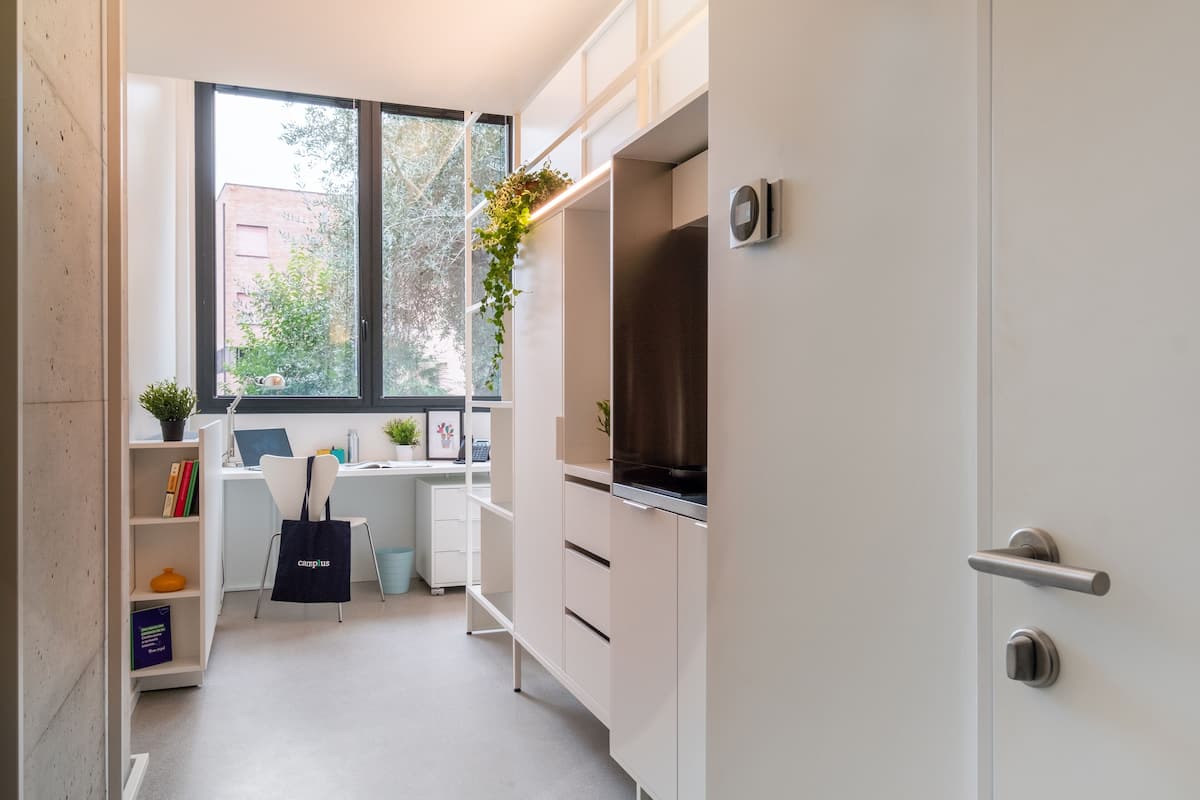 A modern kitchen with white cabinets, a built-in oven, and a window with a view of a brick building.