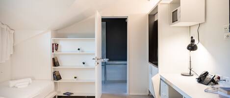 Une chambre moderne avec un lit, un bureau et une chaise. On y trouve également une bibliothèque et une porte qui donne sur une autre pièce.