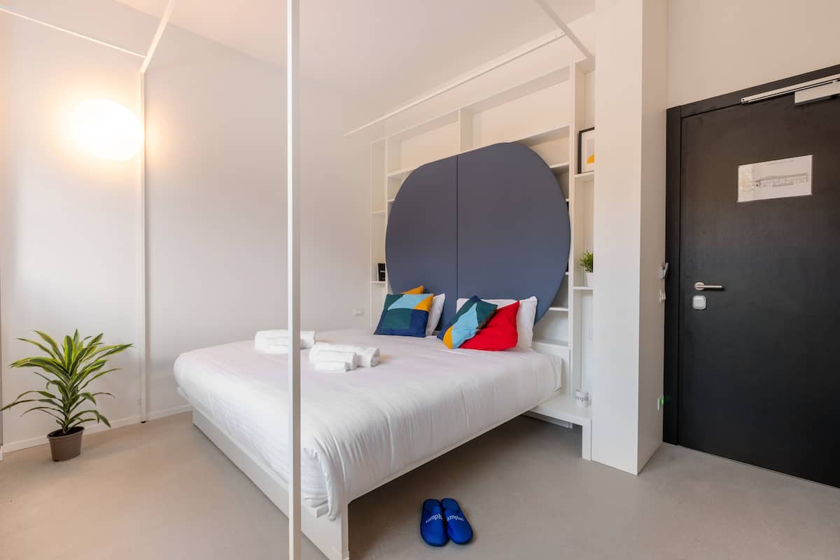 A modern bedroom with a bed, a potted plant, and a pair of shoes on the floor.