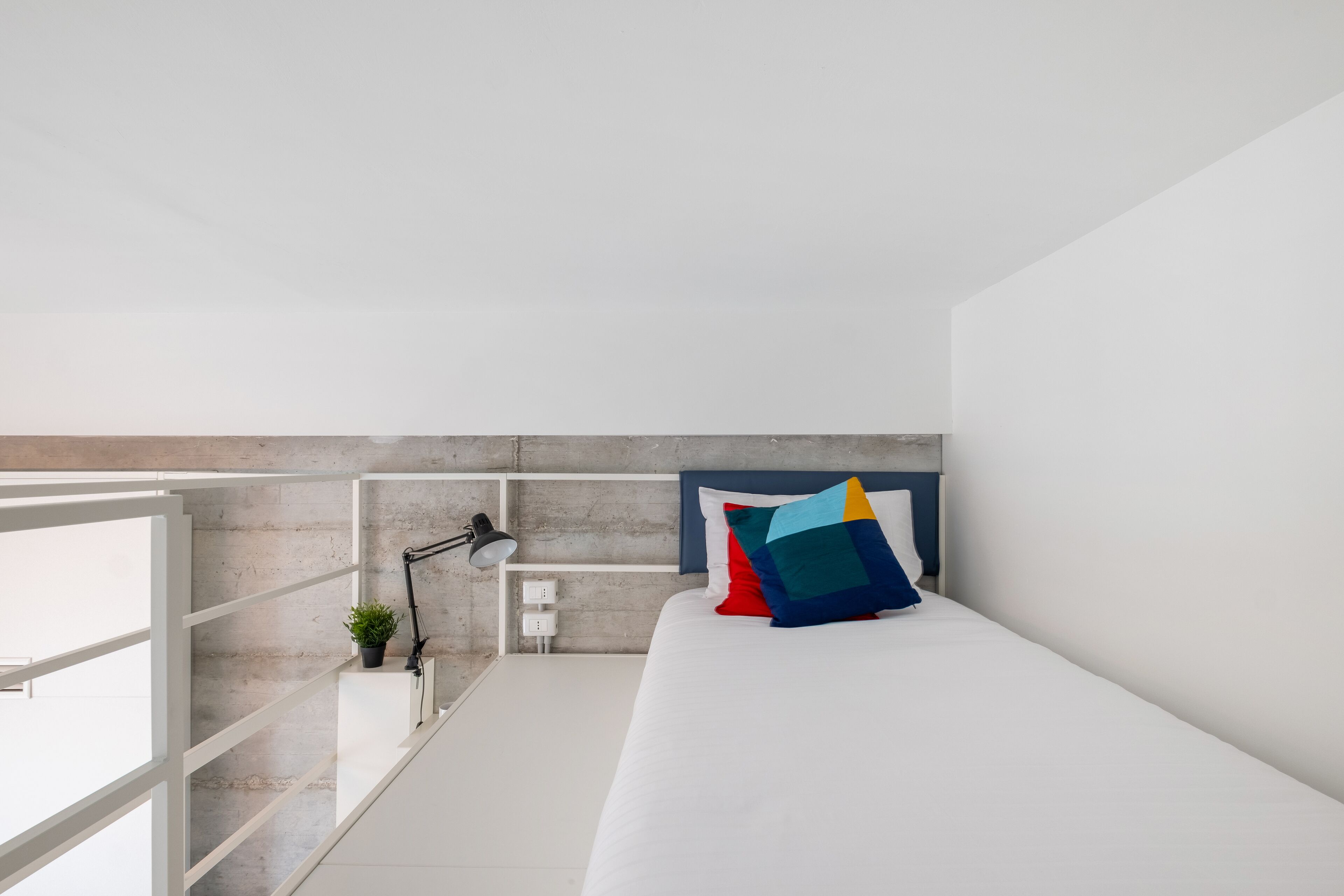 Quarto moderno com cama, escrivaninha com luminária e planta em vaso.