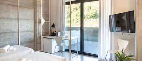 Une chambre d’hôtel moderne dotée d’une grande porte-fenêtre coulissante donnant sur un balcon, d’un bureau avec une chaise, d’un lit avec des serviettes pliées et d’une plante en pot.