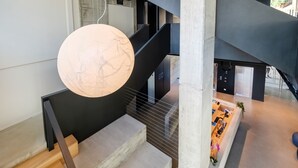 Un interior moderno con una escalera, una lámpara esférica grande y una recepción con escritorio y plantas.