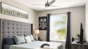 Ein Schlafzimmer mit einem großen Bett, einem Deckenventilator, einem Schreibtisch mit Computer und einem Fenster mit Vorhängen.