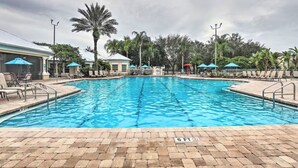 Ein Pool mit Liegestühlen und Sonnenschirmen, umgeben von Palmen und einem bewölkten Himmel.