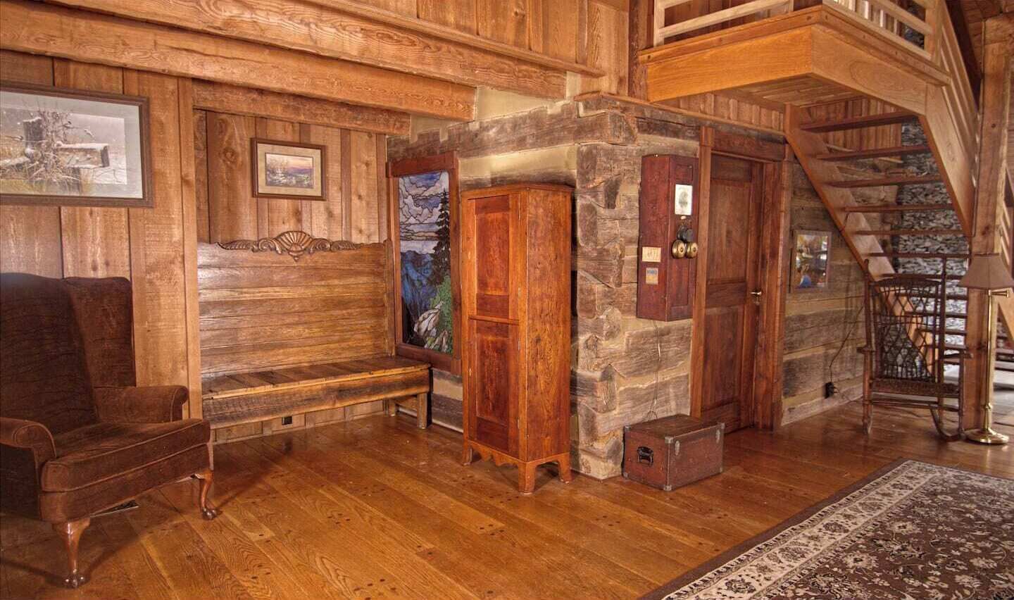 Un intérieur rustique avec des éléments en bois, notamment un banc, un mur en pierre, un escalier et un tapis.