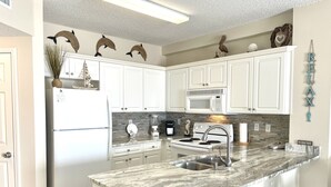 A kitchen with white cabinets, a granite countertop, a refrigerator, a microwave, a stove, and a sink.