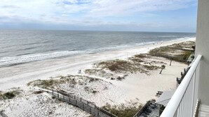 A beach view from a balcony with a wooden deck and outdoor seating.