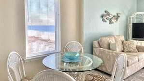 A living room with a round glass table, white wicker chairs, a beige sofa, and a TV on a white stand.