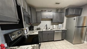 Una cocina con armarios grises oscuros, un refrigerador de acero inoxidable, una estufa negra y una encimera de mármol.