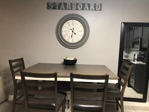 Enjoy meals in this dining area with a table and four chairs, a wall-mounted clock, and a doorway to the adjacent kitchen.