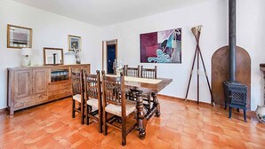 A dining area with a wooden table and chairs, a cabinet, a painting, and a wood-burning stove. - Villa Provenza, Cozy villa with pool near Port Pollensa (Port de Pollença)