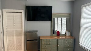 Ein Zimmer mit Holzboden, einem grünen Schrank mit Schubladen, einem flachbildfernseher an der Wand und einem Fenster mit Jalousien.
