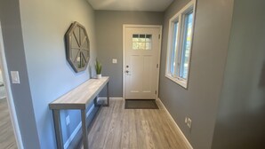 Un couloir avec un banc en bois, une porte dotée d’une fenêtre et un miroir fixé au mur.