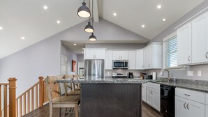 Una cocina moderna con armarios blancos, un refrigerador de acero inoxidable y una encimera de granito.