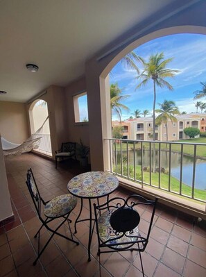 Relax on the balcony with a hammock, chair, and table, taking in the serene views of the water and palm trees.