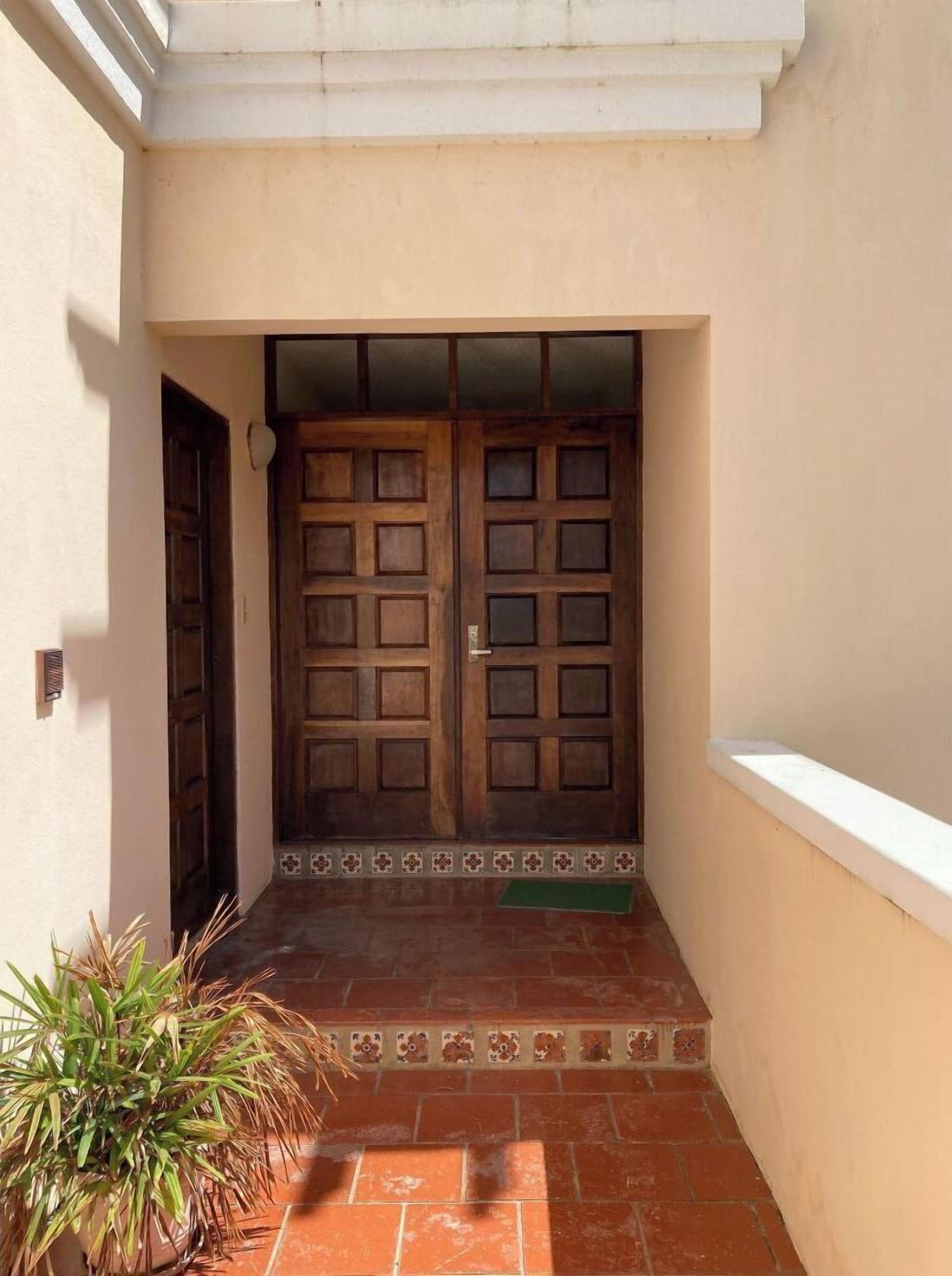 A building entrance with two wooden doors, a tiled floor, and a potted plant.