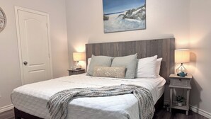 Un dormitorio con una cama grande, dos mesitas de noche con lámparas, una puerta y un cuadro en la pared.