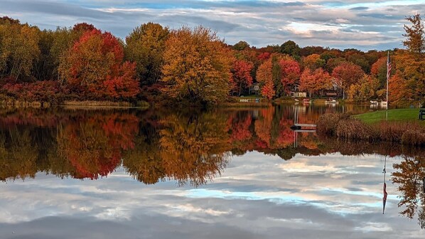 Un lac paisible, dont les eaux reflètent les couleurs automnales du feuillage environnant, bordé d’arbres et doté d’un petit quai.