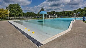 A large outdoor swimming pool with a blue canopy structure, surrounded by trees and a fenced area.