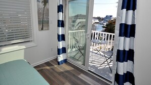 Un balcón con vistas a un puerto deportivo, una puerta de cristal y una pequeña mesa con dos copas de vino.