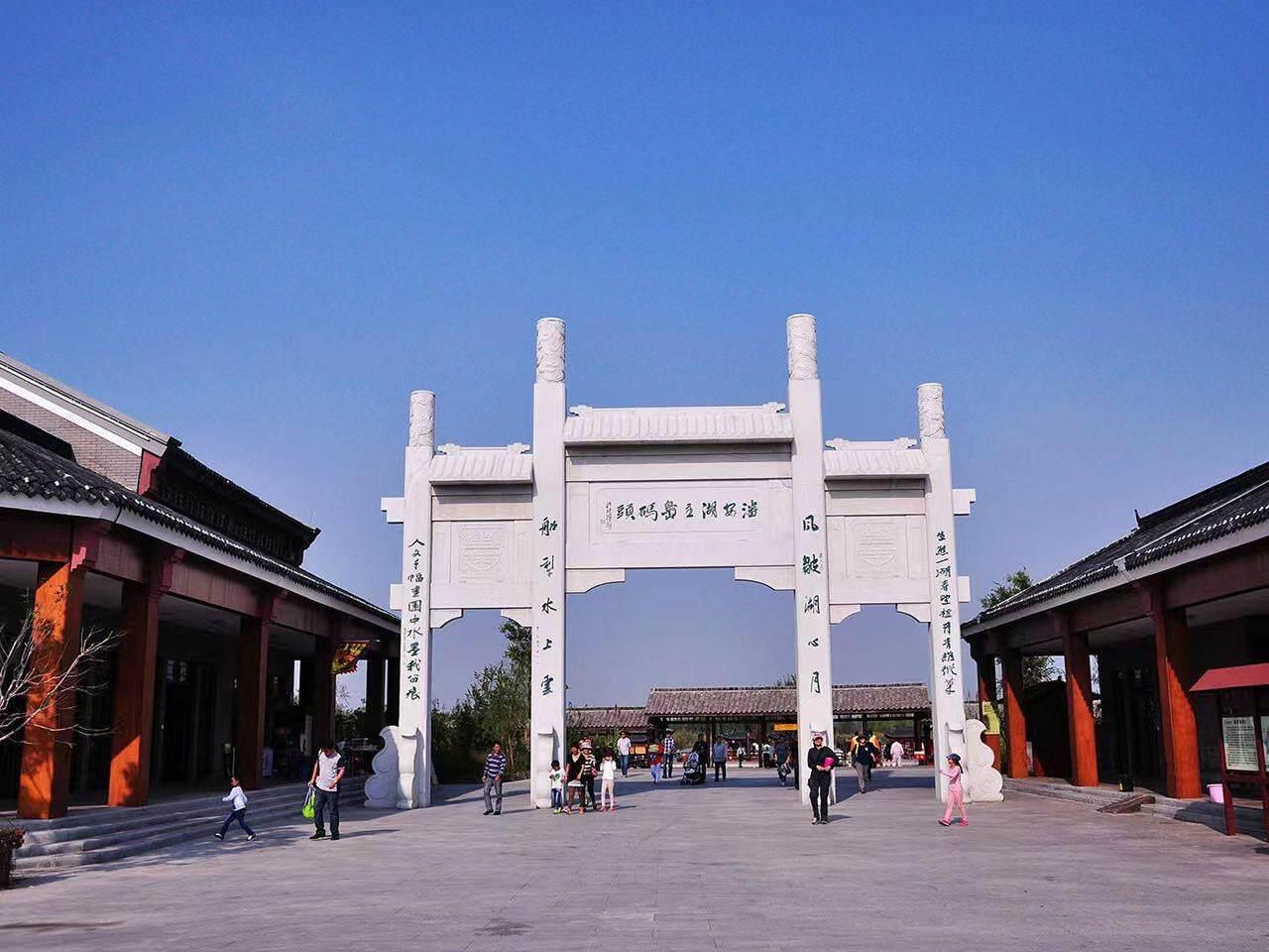 A traditional Chinese gate with inscriptions, surrounded by visitors and traditional architecture.