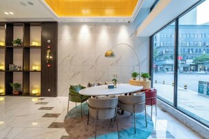Un moderno vestíbulo de hotel con una mesa redonda, sillas, una estantería y un ventanal con vistas a la ciudad.