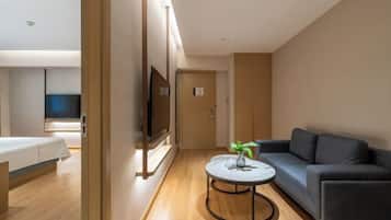 A modern hotel room with a bed, a sofa, a small round table, and a TV mounted on the wall.
