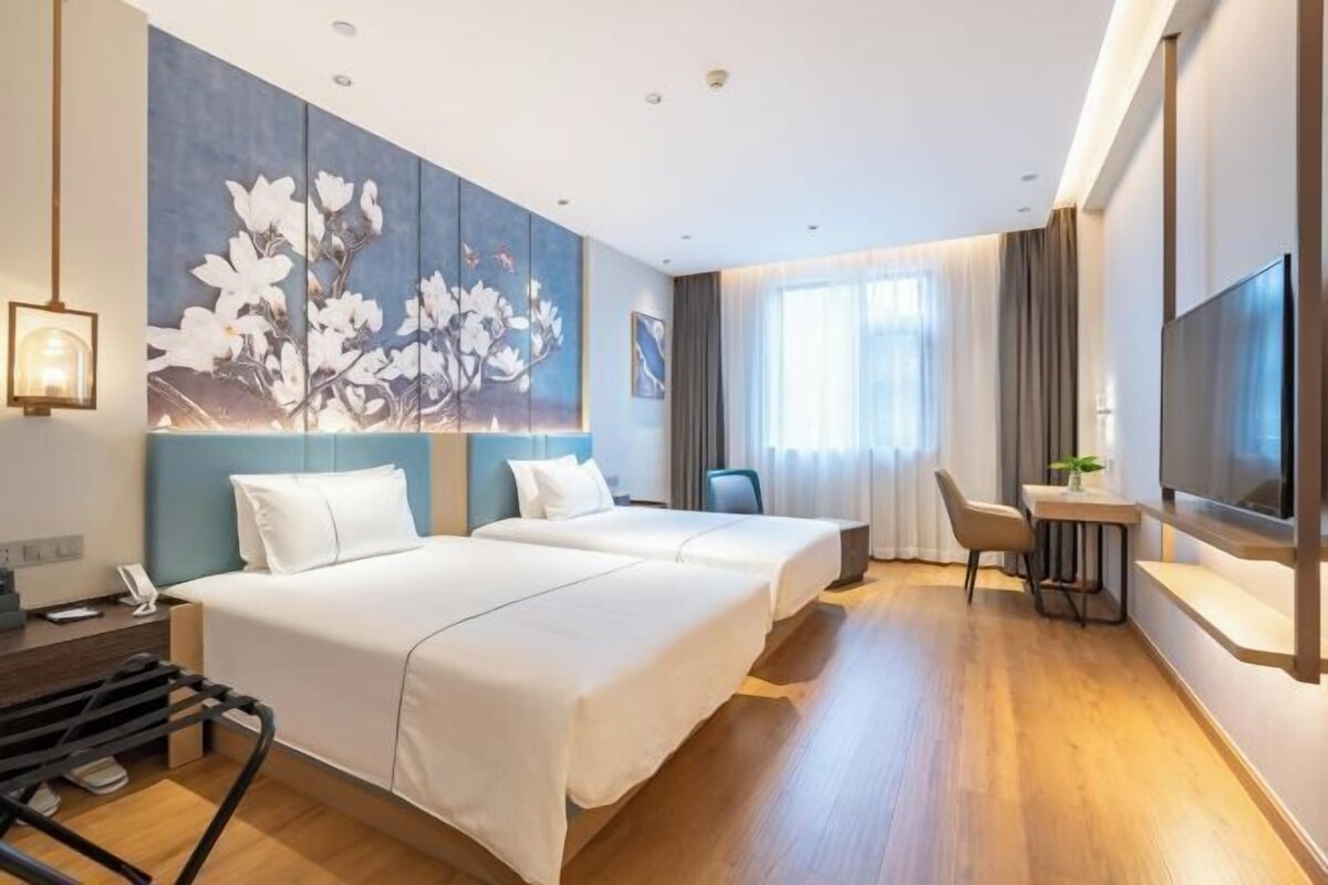 A hotel room with two beds, a desk, a chair, a TV, and a large floral artwork on the wall.