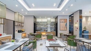 A modern dining area with multiple tables and chairs, a central kitchen area, and a view of the kitchen through glass partitions. - Magnotel Hotel (Xuzhou Suning Plaza) (Xuzhou)
