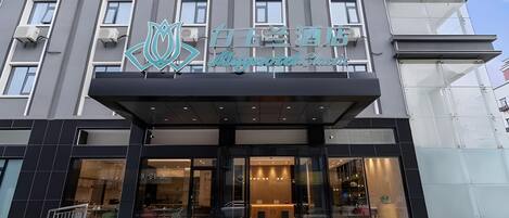 Een hotelentree met een modern ontwerp, met een opvallend logo boven de ingang en een glazen gevel.