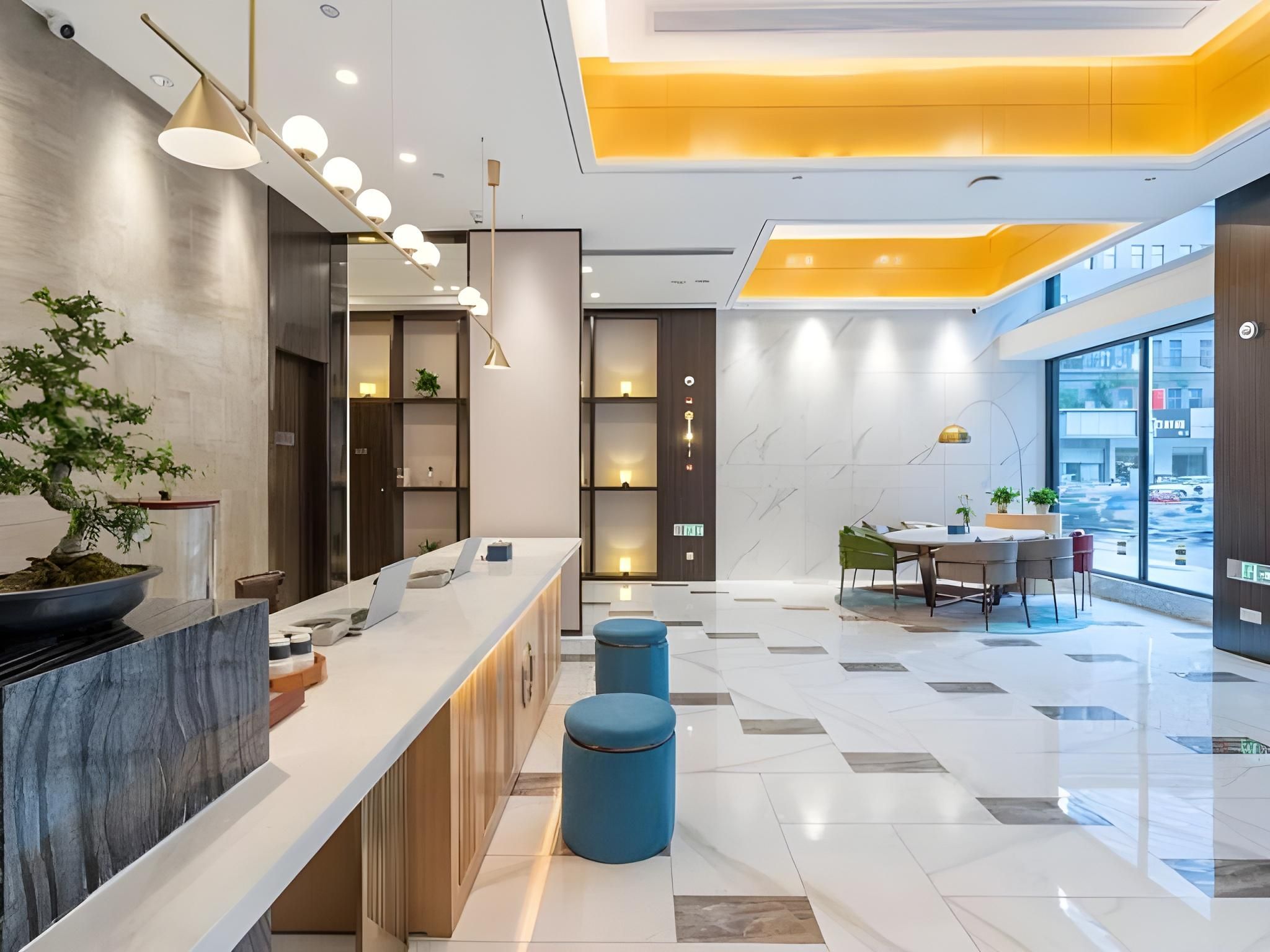 Un hall d’hôtel moderne doté d’un comptoir d’accueil, d’un espace salon et de grandes fenêtres donnant sur la rue.