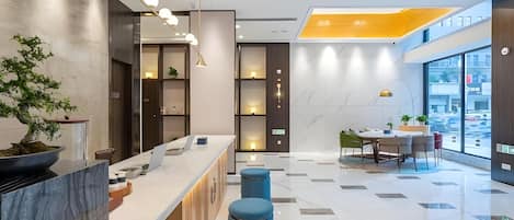 A modern hotel lobby with a reception desk, seating area, and large windows offering a view of the street.