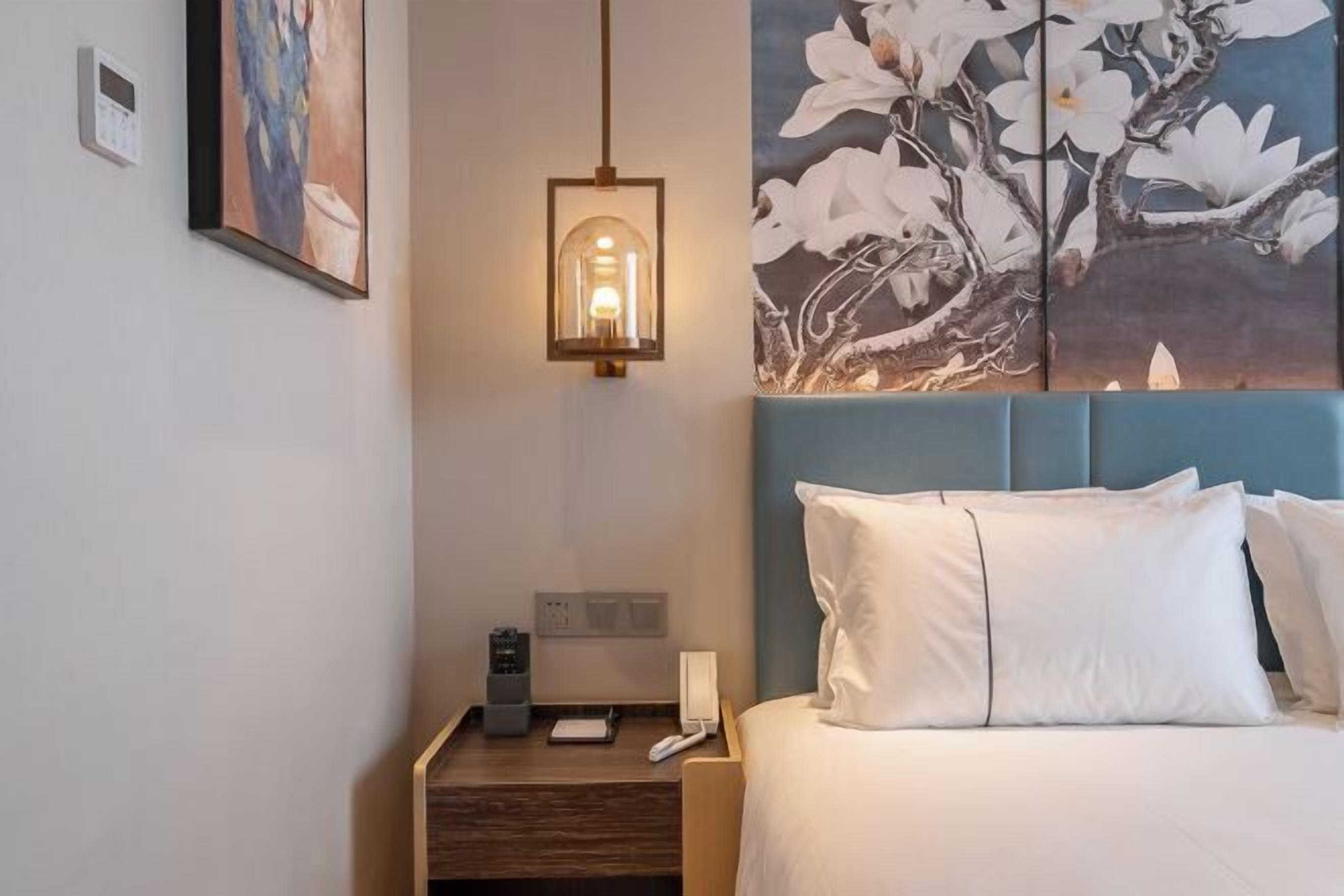 A hotel room with a bed, bedside table, lamp, and artwork on the wall.
