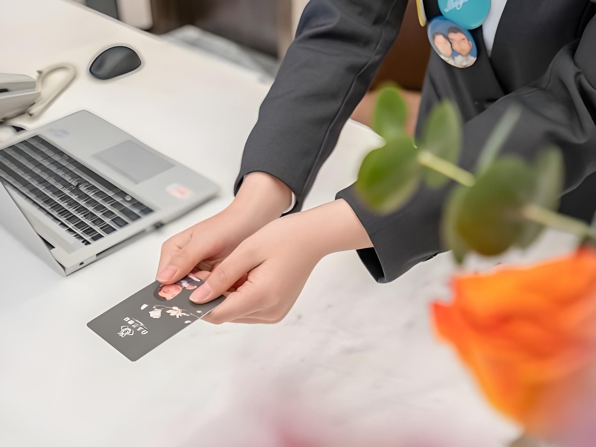A person placing a card on a desk with a laptop and a mouse.