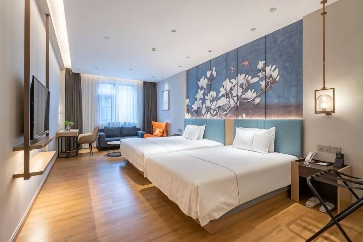 A hotel room with two beds, a desk, a chair, a TV, and a painting on the wall.