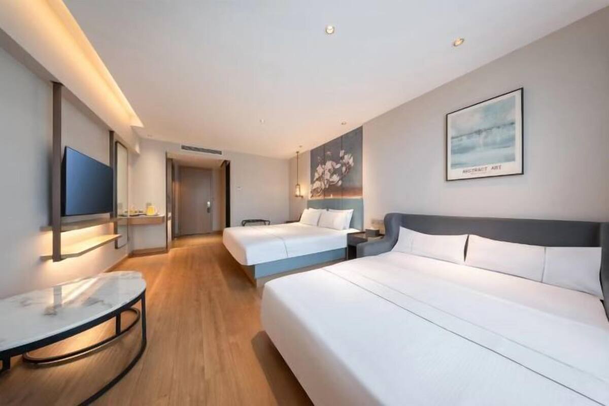 A hotel room with two beds, a TV, a desk, and artwork on the walls.
