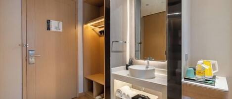 A modern bathroom with a wooden door, a bench, a sink with a mirror, and a shelf with towels and toiletries.