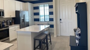 A modern kitchen with white cabinets, a stainless steel refrigerator, a built-in oven, and a large island with bar stools.