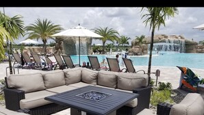 A poolside area with a large black fire pit table, wicker lounge chairs, and a waterfall feature in the background.