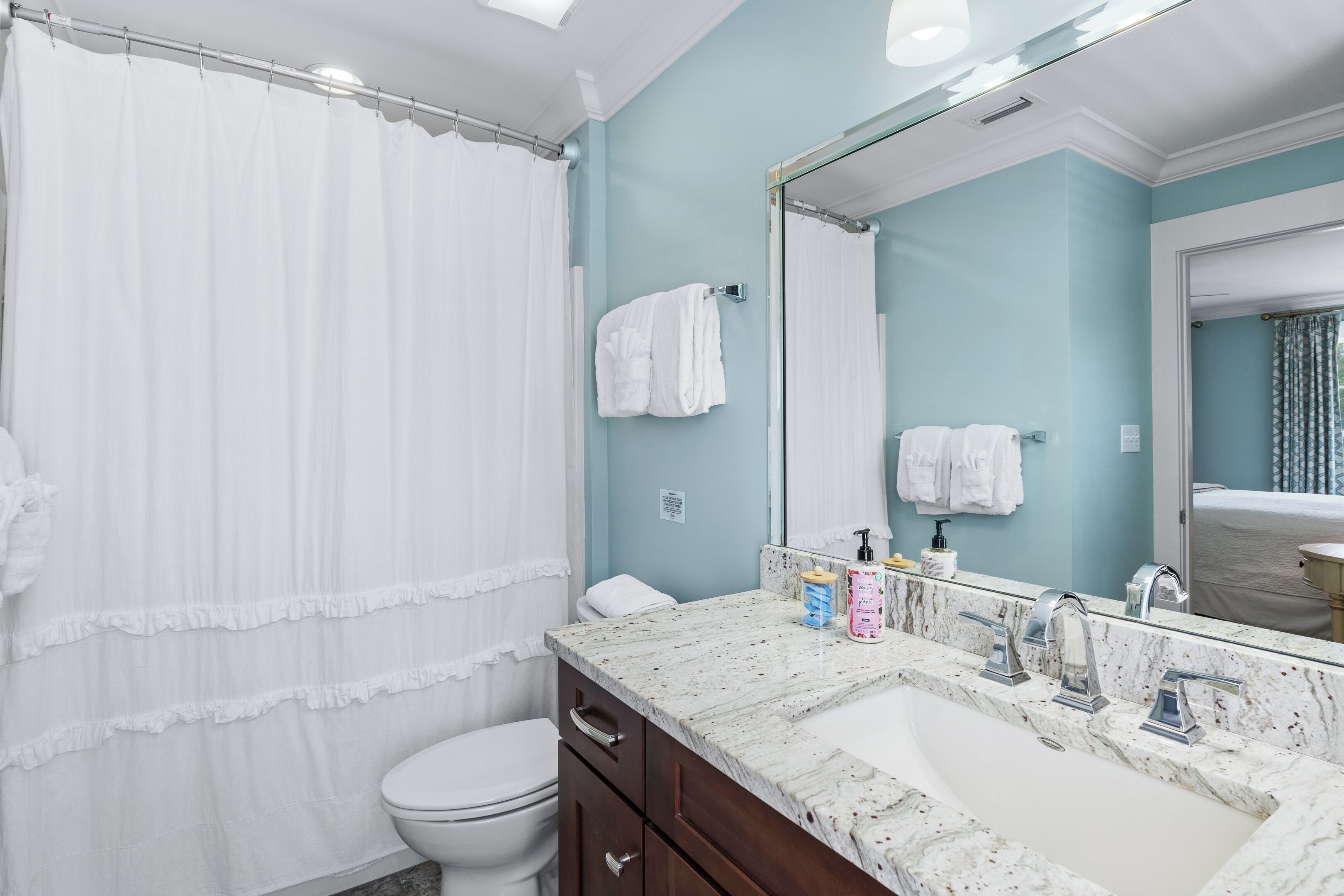Un baño con inodoro blanco, cortina de ducha, lavabo con encimera de mármol y espejo.
