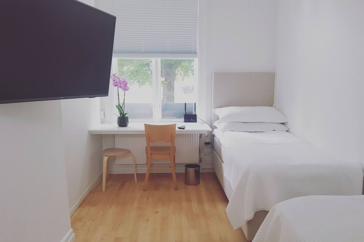 A small, tidy room with a bed, a desk with a chair, a potted plant, and a window.