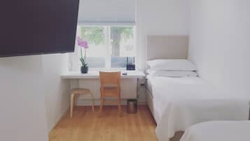 A small, tidy room with a bed, a desk with a chair, a potted plant, and a window.