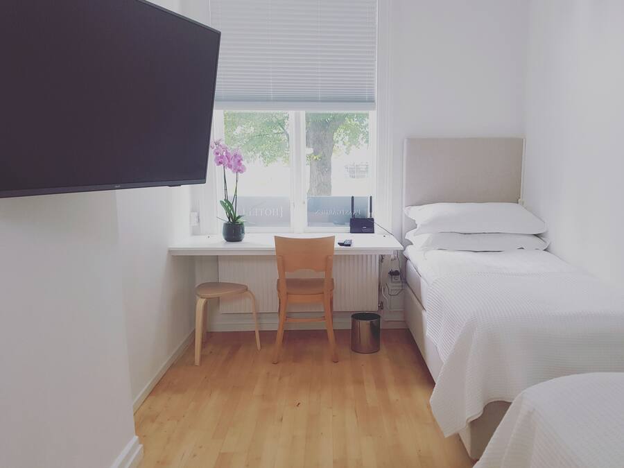 A small, tidy room with a bed, a desk with a chair, a potted plant, and a window.