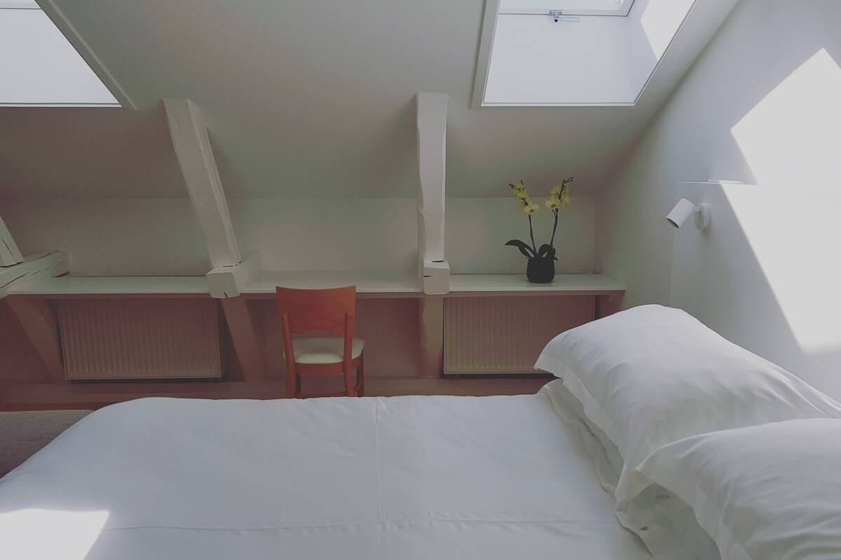 A bedroom with a bed, a desk, a chair, and a window.