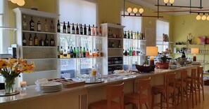 A bar area with shelves of liquor bottles, a variety of glasses, and a counter with bar stools.