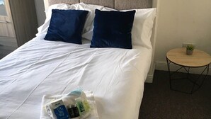 A neatly made bed with white linens and two dark blue pillows, a small round table with a plant, and a framed picture on the wall. - Townhouse @ Victoria Road Stoke (Stoke-on-Trent)