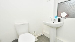 A small, clean bathroom with a toilet, sink, and mirror. - Townhouse @ Victoria Road Stoke (Stoke-on-Trent)
