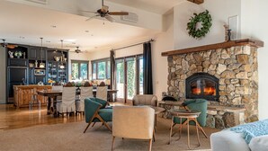 Amplia sala de estar con chimenea de piedra, comedor y cocina al fondo, además de un ventilador de techo.
