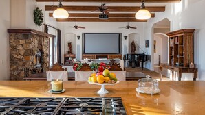 Un salón espacioso con chimenea de piedra, zona de comedor con una mesa dispuesta para dos personas, un piano y una pantalla de televisión grande.