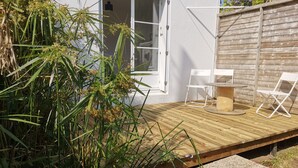A wooden deck with a table and two white chairs, surrounded by lush greenery.